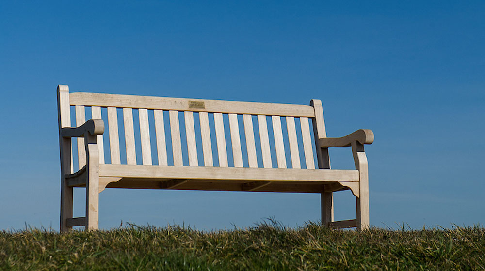 Photo of an empty park bench with a blue sky